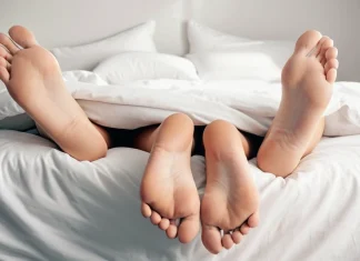 The Ultimate Diet That Will Transform Your Energy Levels and Sex Life Two pairs of bare feet peeking out from under white duvet bedding in cozy morning bed