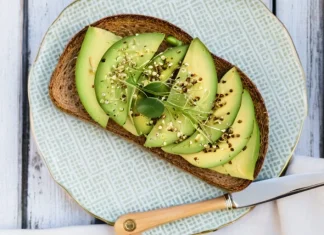 Foods To Keep Your Heart Healthy and Lower Your Cholesterol Avocado sourdough toast topped with fresh microgreens and hemp seeds on ceramic plate