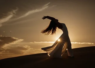 Gifts Of The Divine Feminine Silhouette of woman in flowing white dress dancing on sand dunes during golden sunset