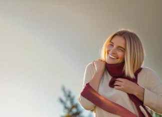 Ways You May Be Sabotaging Your Happiness Joyful woman in cream sweater smiling warmly outdoors in golden sunlight