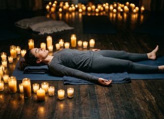 What Is Yoga Nidra? The Science Behind the Practice That Works While You Sleep Woman lying in savasana position practicing yoga nidra surrounded by glowing candles
