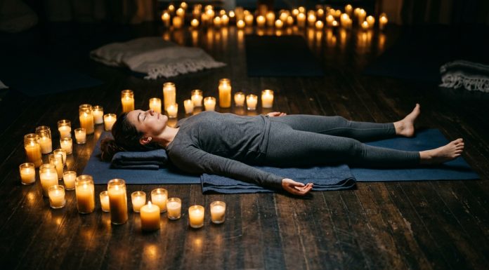 What Is Yoga Nidra? The Science Behind the Practice That Works While You Sleep Woman lying in savasana position practicing yoga nidra surrounded by glowing candles